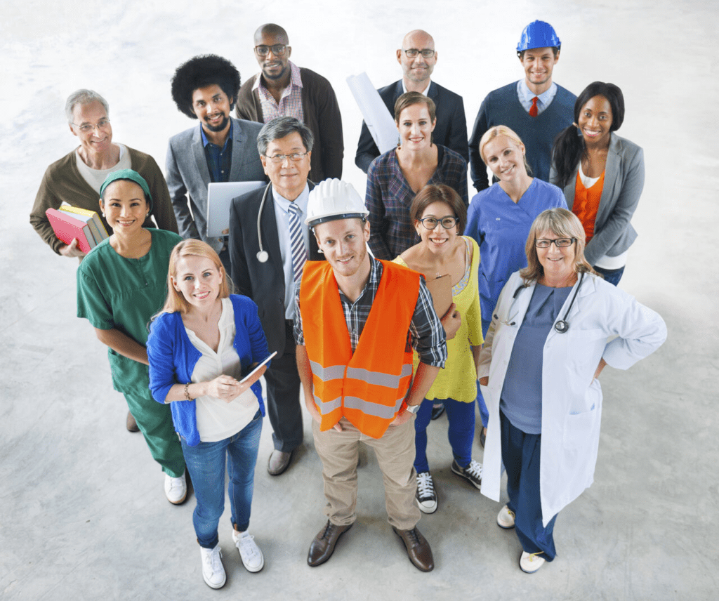 Grupo diverso de profissionais posando juntos, representando diferentes áreas de atuação, incluindo saúde, engenharia, educação, construção civil e outros setores, todos sorrindo e olhando para a câmera em um ambiente claro.