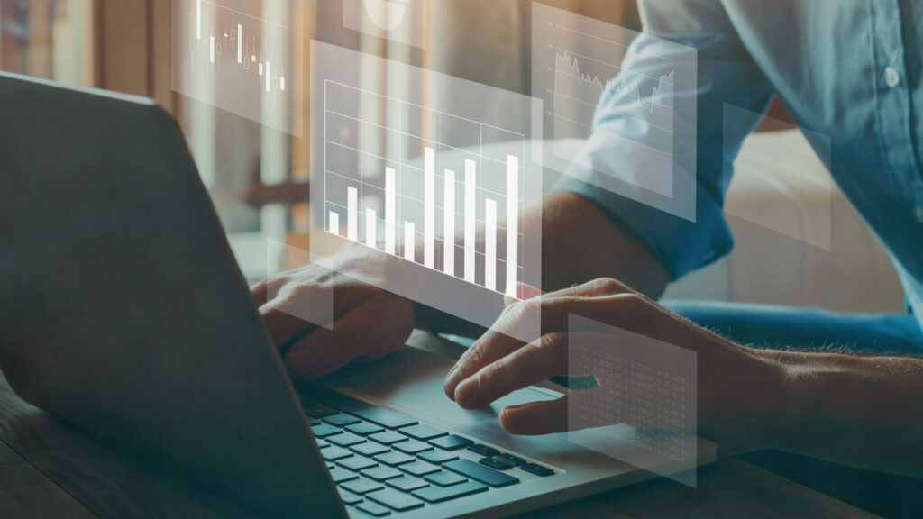 Imagem de uma pessoa utilizando um computador, com gráficos, números e ícones de dados flutuando ao redor da tela, simbolizando o processo de análise de Big Data. A imagem sugere a interação entre o usuário e grandes volumes de informação, representando a coleta e interpretação de dados em tempo real. O fundo tecnológico e os elementos visuais destacam a importância da análise de dados para a tomada de decisões estratégicas e eficientes.