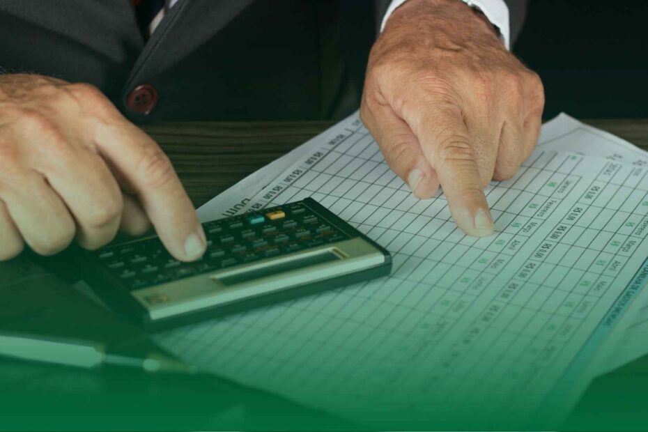 Mãos de pessoa usando calculadora e apontando para planilha de pagamentos, representando a análise de processos trabalhistas e controle financeiro empresarial.