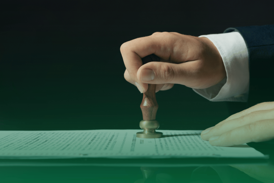 Mão carimbando documento oficial sobre uma mesa, simbolizando aprovação jurídica ou validação contratual.